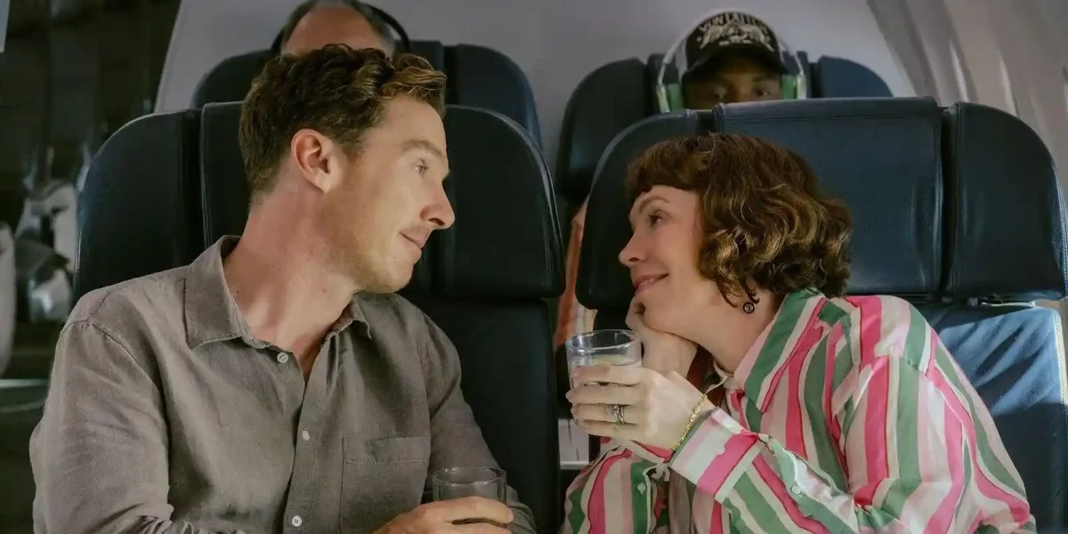 benedict cumberbatch and olivia colman sitting on a plane and smiling dreamily at each other in the roses